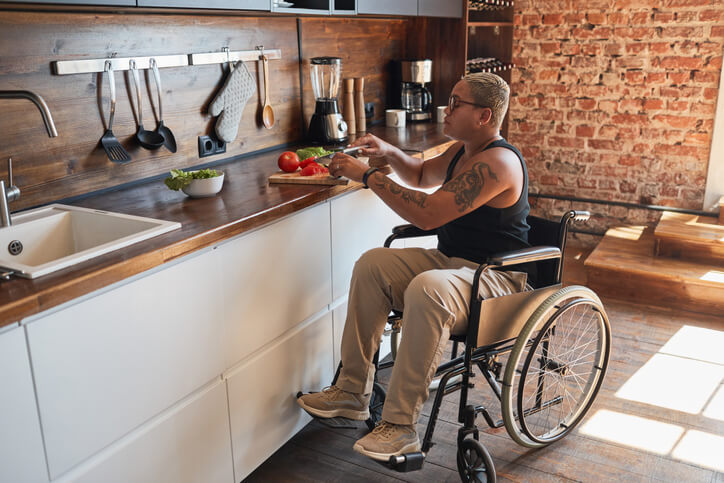 osoba na wózku inwalidzkim przygotowująca jedzenie w kuchni